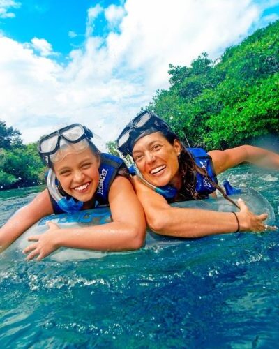 Visitors relaxing in inner tubes floating down a serene river surrounded by tropical vegetation at Xel-Há Park.