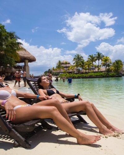 Lounge chairs under umbrellas on a sandy beach at Xcaret Park, offering a relaxing spot for visitors to unwind.