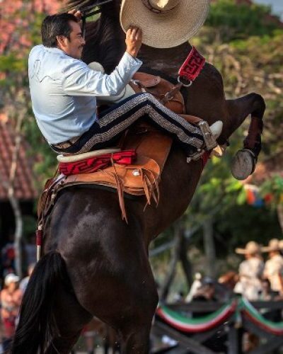 Equestrian show at Xcaret Park featuring skilled riders performing stunts on horseback in traditional Mexican attire.