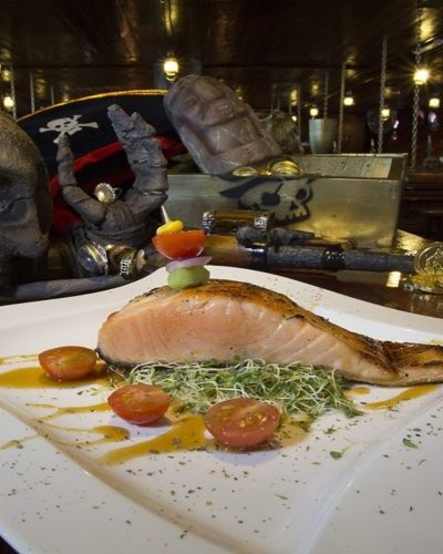 Grilled salmon fillet served with herbs and vegetables, part of the gourmet dining experience on the Jolly Roger pirate ship.