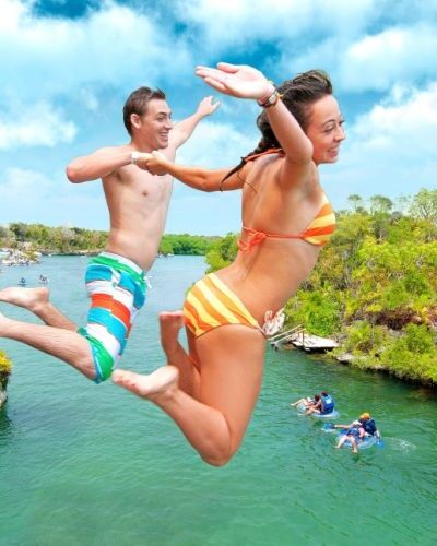 Traveler diving into clear turquoise water from a cliff at Xel-Há Park, surrounded by tropical scenery in Mexico.