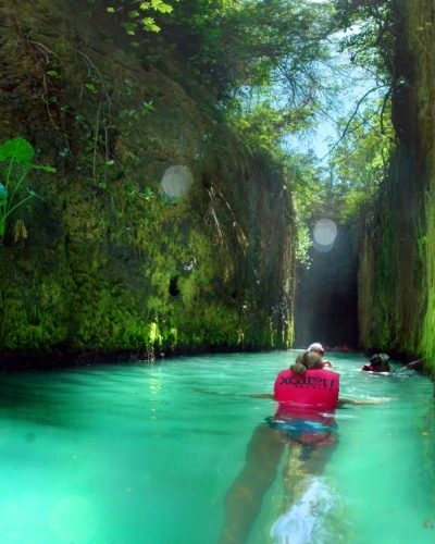 Person floating in a serene underground river with natural light filtering through rock openings at Xcaret Park.