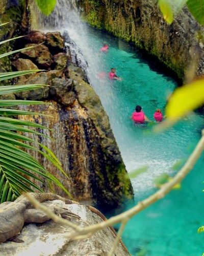 Swimmers exploring a scenic underground river surrounded by impressive rock formations at Xcaret Park.