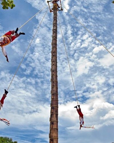 Voladores de Papantla performers swinging from a tall pole in a traditional Mexican ceremony at Xcaret Park.