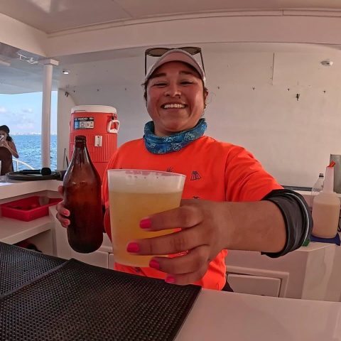 On board the catamaran Baby Dancer, a smiling waiter is serving a glass of Corona beer.