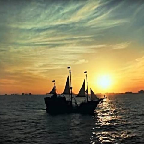 The Jolly Roger pirate ship at sunset in Cancun Bay, creating a picturesque view against the golden sky and tranquil water.