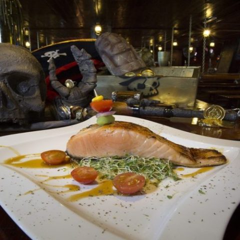 Grilled salmon fillet served with herbs and vegetables, part of the gourmet dining experience on the Jolly Roger pirate ship.