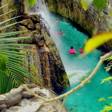 Swimmers exploring a scenic underground river surrounded by impressive rock formations at Xcaret Park.